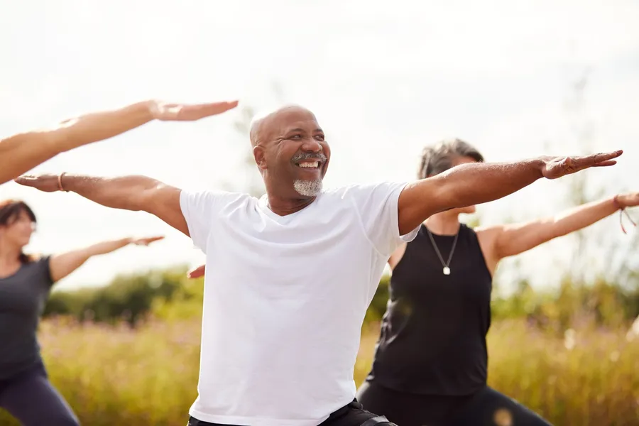 A smiling man stretching his arms wide in an outdoor class