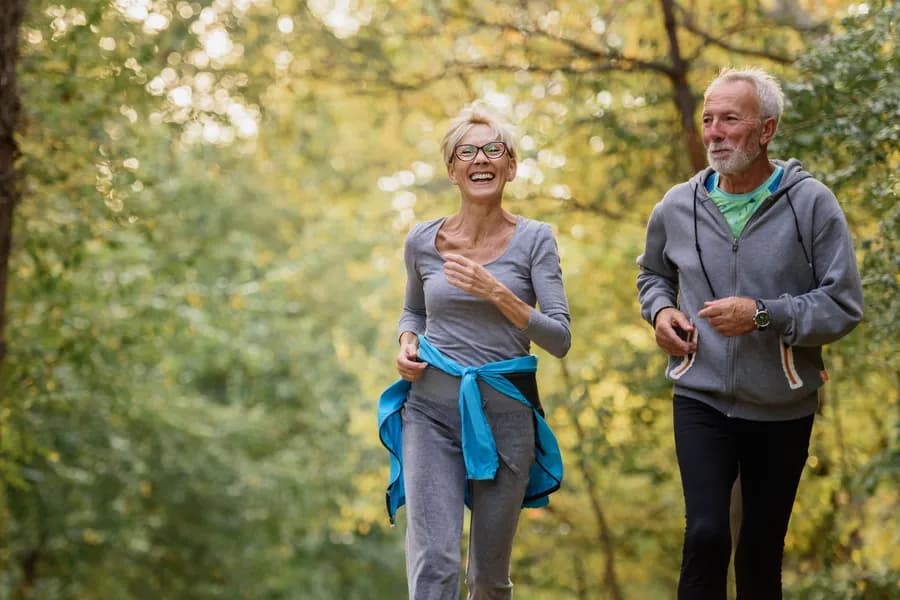 An older couple jogging together through a park