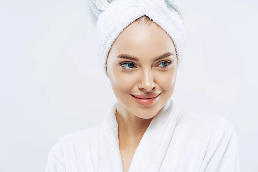 A woman in a robe and hair towel with clear, healthy skin