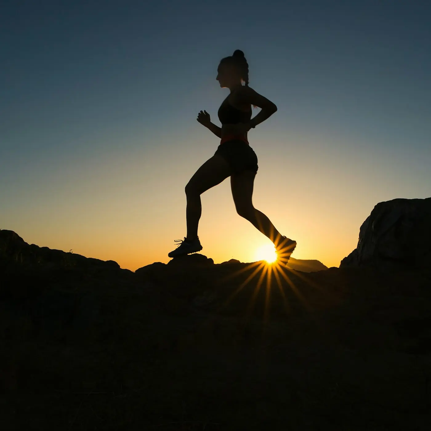 A runner in silhouette on a rocky trail against a low sun