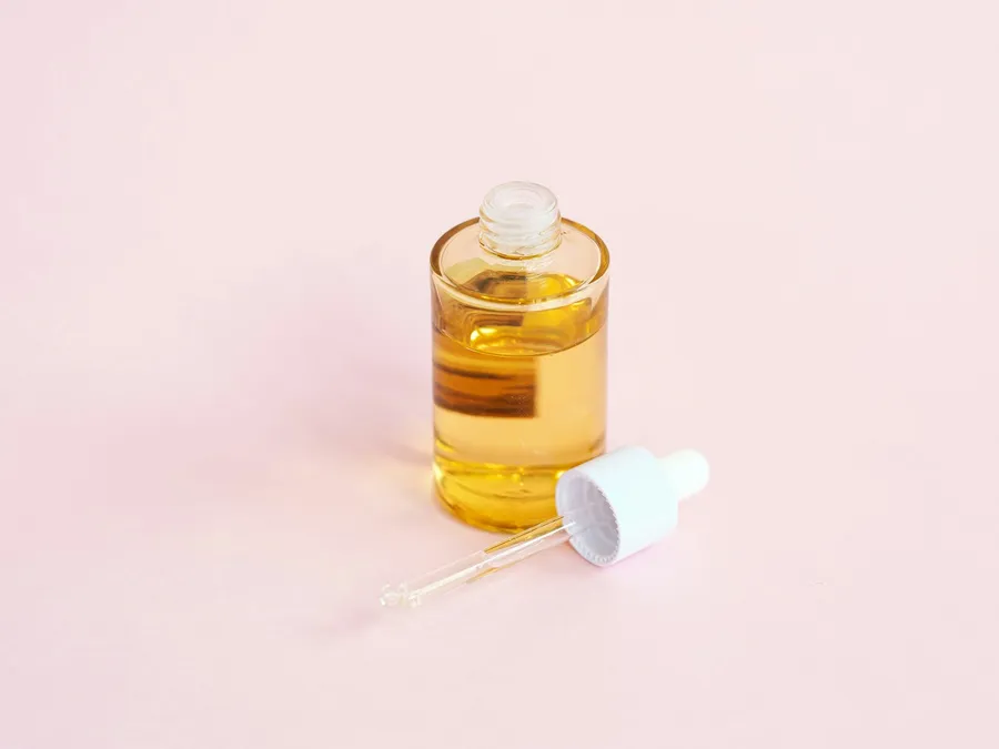 An open glass bottle of golden serum beside its dropper