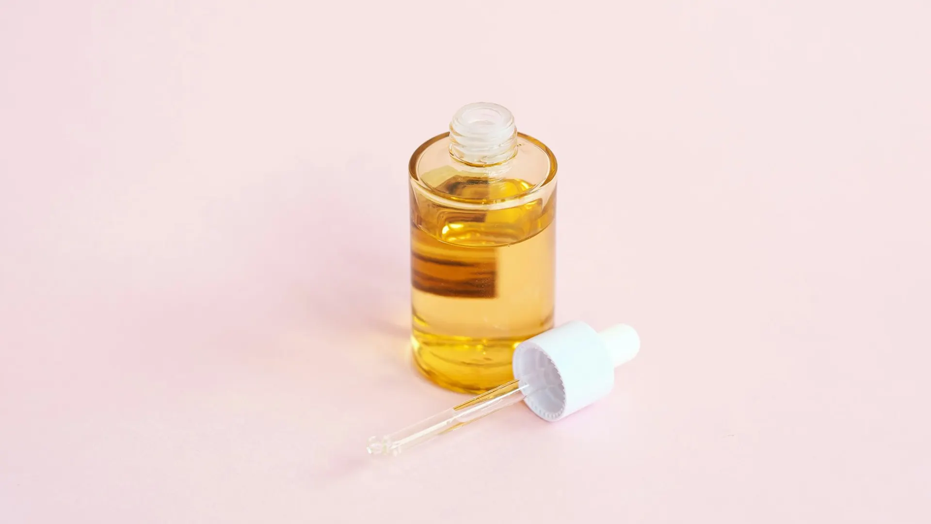 An open glass bottle of golden serum with its dropper resting beside it