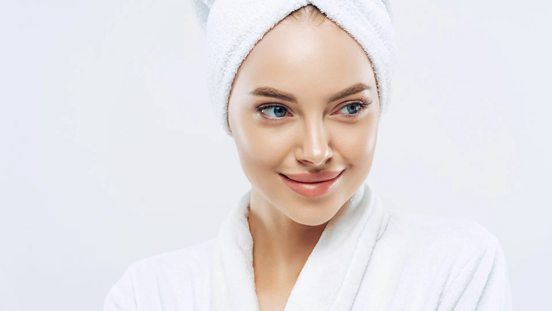 A smiling woman in a white robe with her hair wrapped in a towel