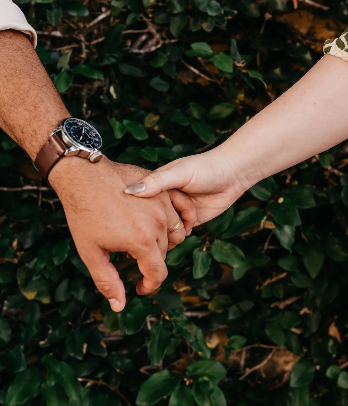 A couple holding hands while walking past a hedge