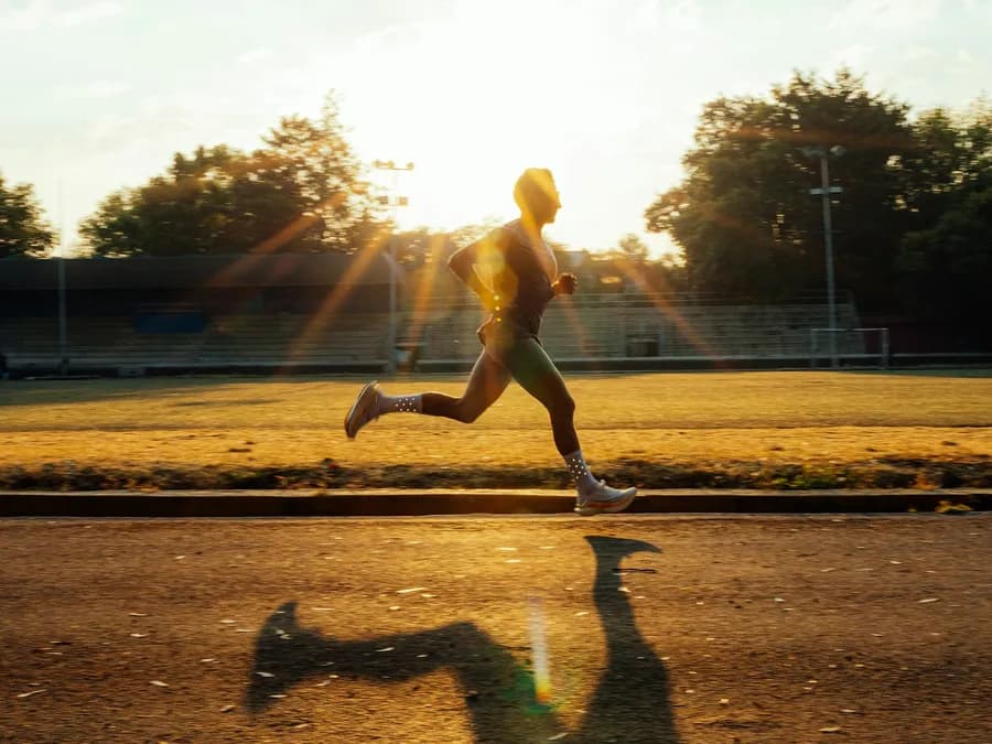 A runner in full stride on a track with the sun low behind