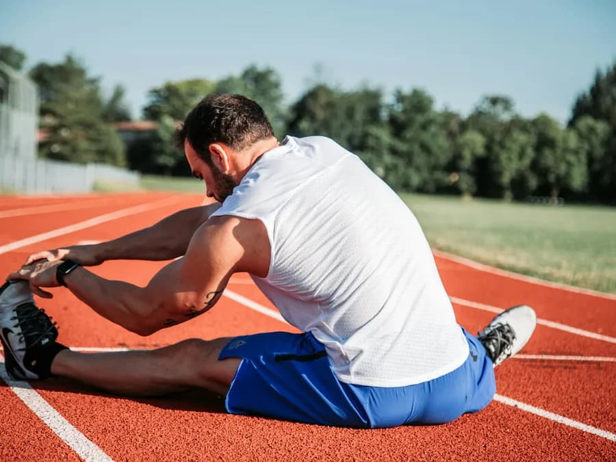 A man seated on a running track stretching toward his foot
