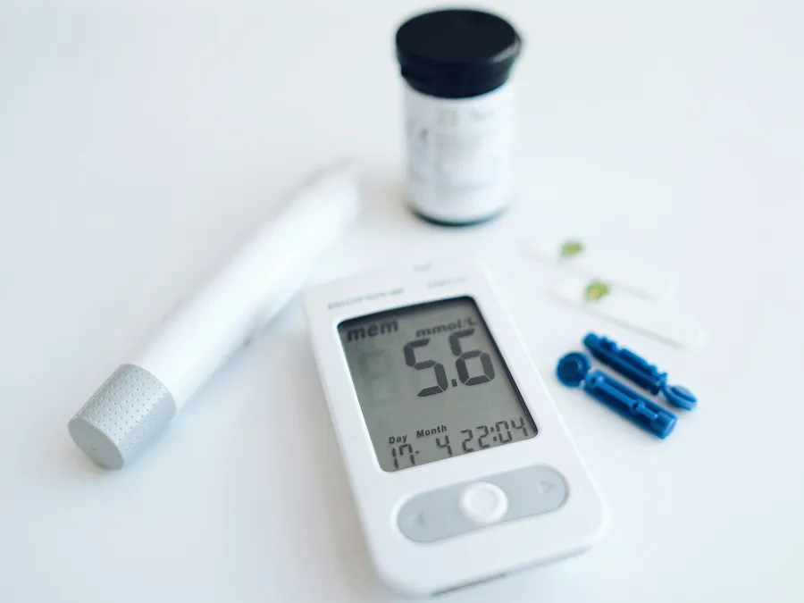 A blood glucose meter reading 5.6 beside a lancing device and test strips